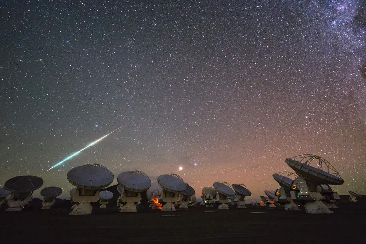 Un bolide trace une ligne lumineuse au-dessus des antennes d'un radiotelescope.