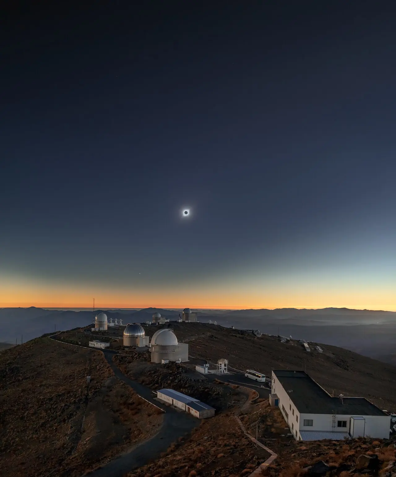 Le Soleil eclipse au-dessus des coupoles d'un observatoire, en plein jour assombri.
